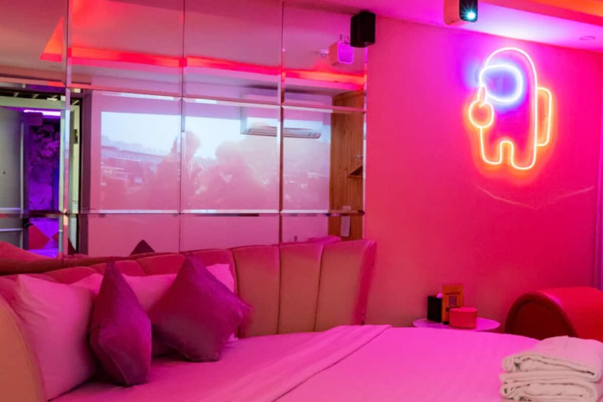 Een moderne slaapkamer met een roze en paarse kleurenschema, neonverlichting en een bed met kussens.