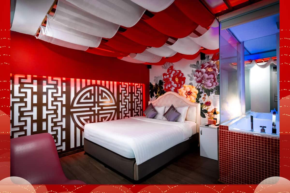 Een moderne slaapkamer met een bed, nachtkastjes, een kaptafel en een wand met een rood-wit patroon.