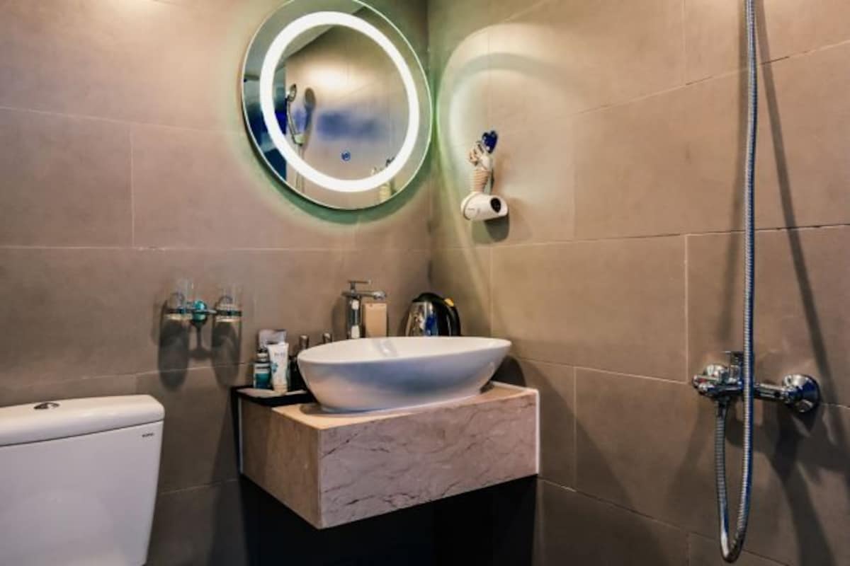 Een moderne badkamer met een groot ovaal wastafel, een ronde spiegel en een handdouche.
