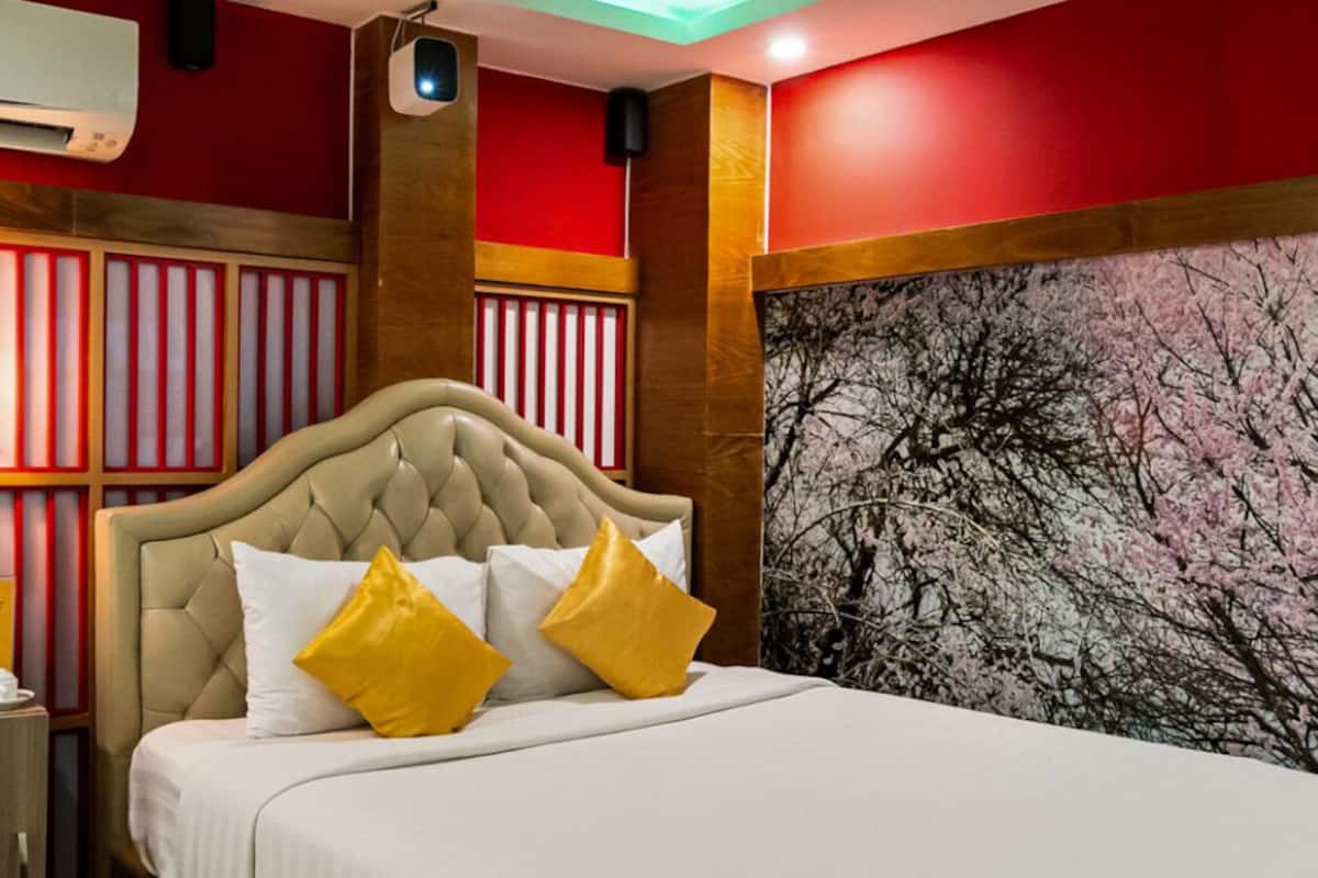 Een hotelkamer met een groot bed, rode muren en een schilderij van bomen.