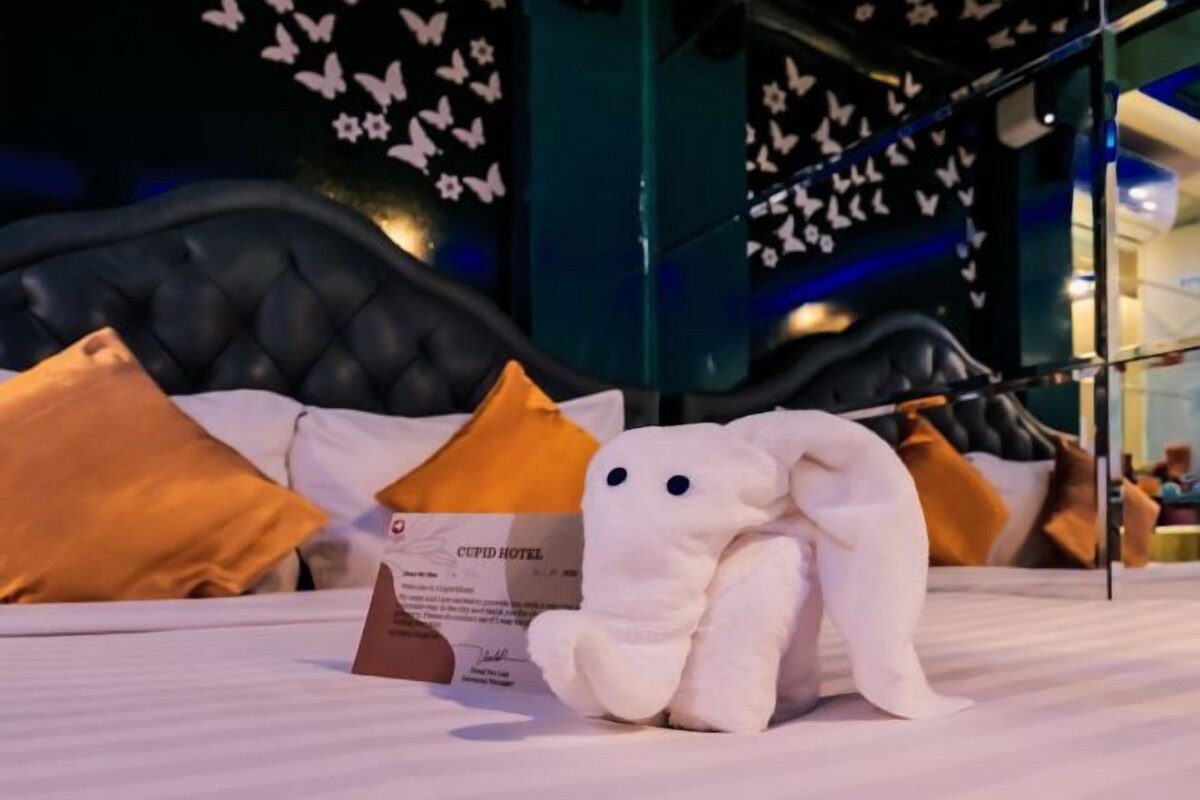 A hotel room with a bed, pillows, a plush toy, and a sign indicating the hotel name.