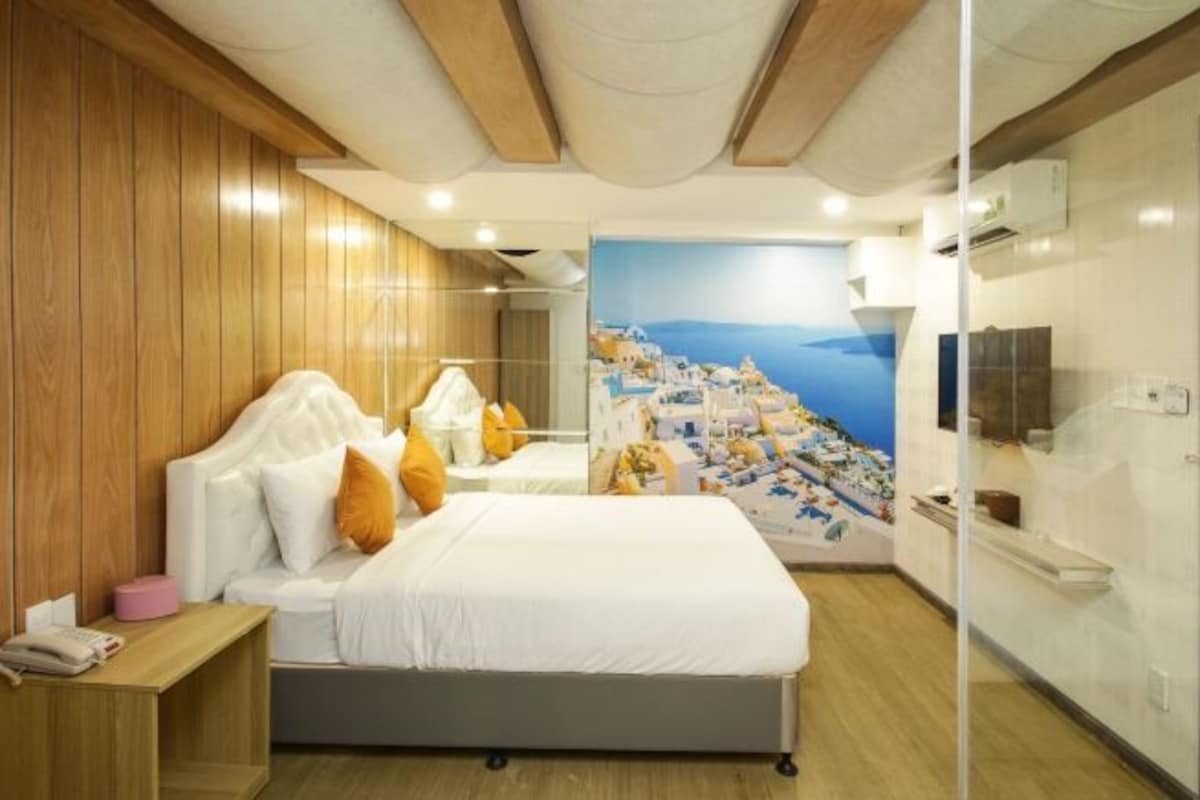 Een hotelkamer met een bed, nachtkastje en een muurschildering van een kustplaats.