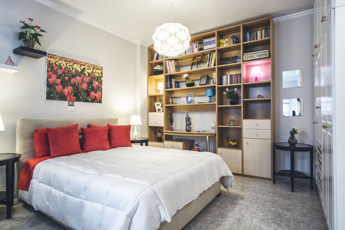 A bedroom with a large bed, a bookshelf, and a painting on the wall.