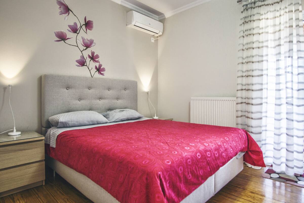 A bedroom with a bed, nightstands, a wall-mounted air conditioner, and a radiator.