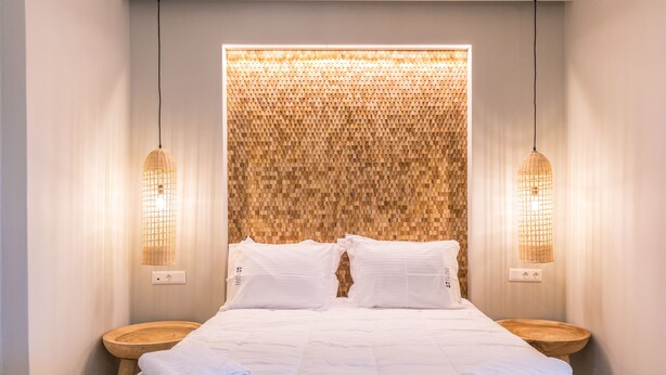 A neatly made bed with white linens and towels, two bedside tables, and a textured wall behind the bed.