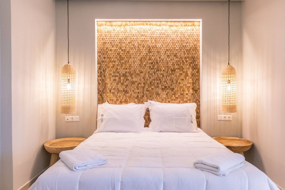 A neatly made bed with white linens and towels, two bedside tables, and a textured wall behind the bed.