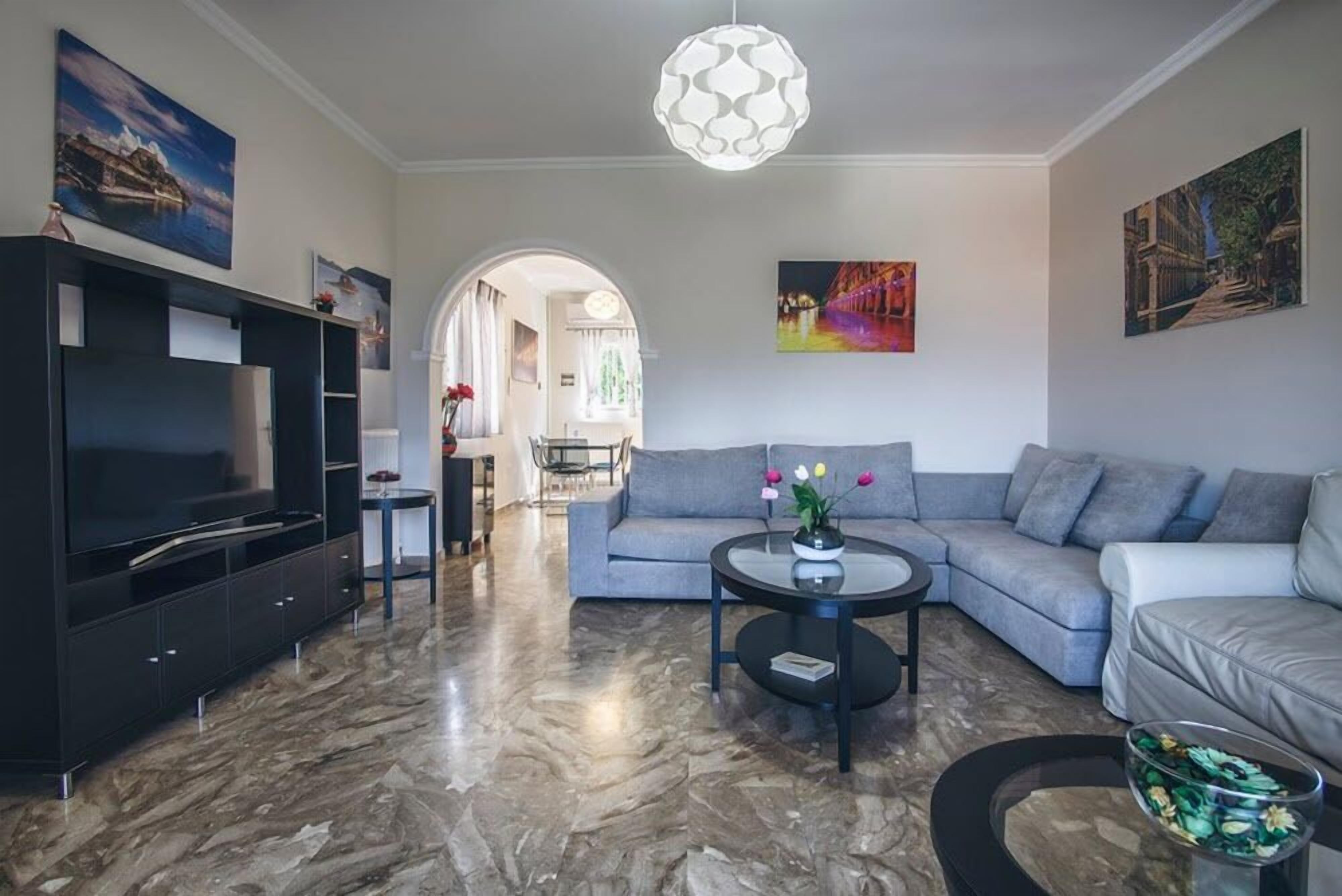 A modern living room with a large flat-screen TV, grey sofas, a coffee table, and artwork on the walls.