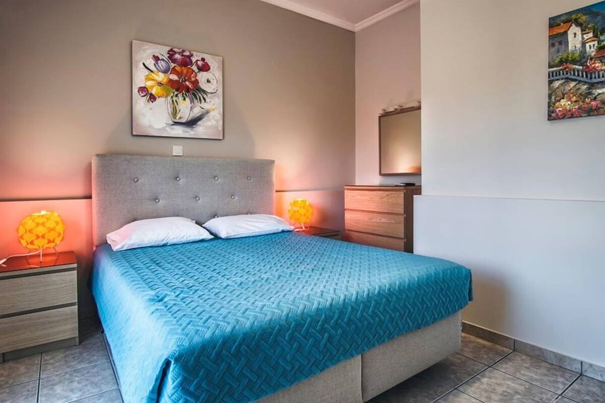 A bedroom with a bed, two bedside tables, a nightstand, a dresser, and two wall-mounted lamps.