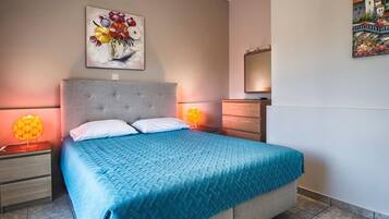 A bedroom with a bed, two bedside tables, a nightstand, a dresser, and two wall-mounted lamps.