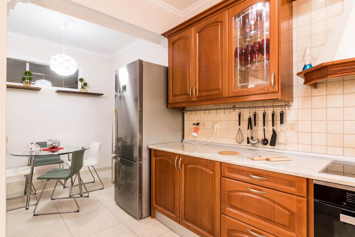 A modern kitchen with wooden cabinets, a stainless steel refrigerator, and a dining area with a glass table and chairs.