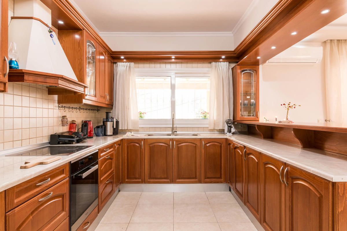 A modern kitchen with wooden cabinets, a built-in oven, and a large window with curtains.