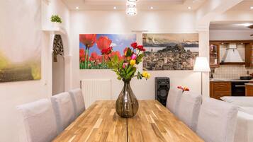 A dining area with a wooden table, cushioned chairs, a vase with flowers, and artwork on the walls.
