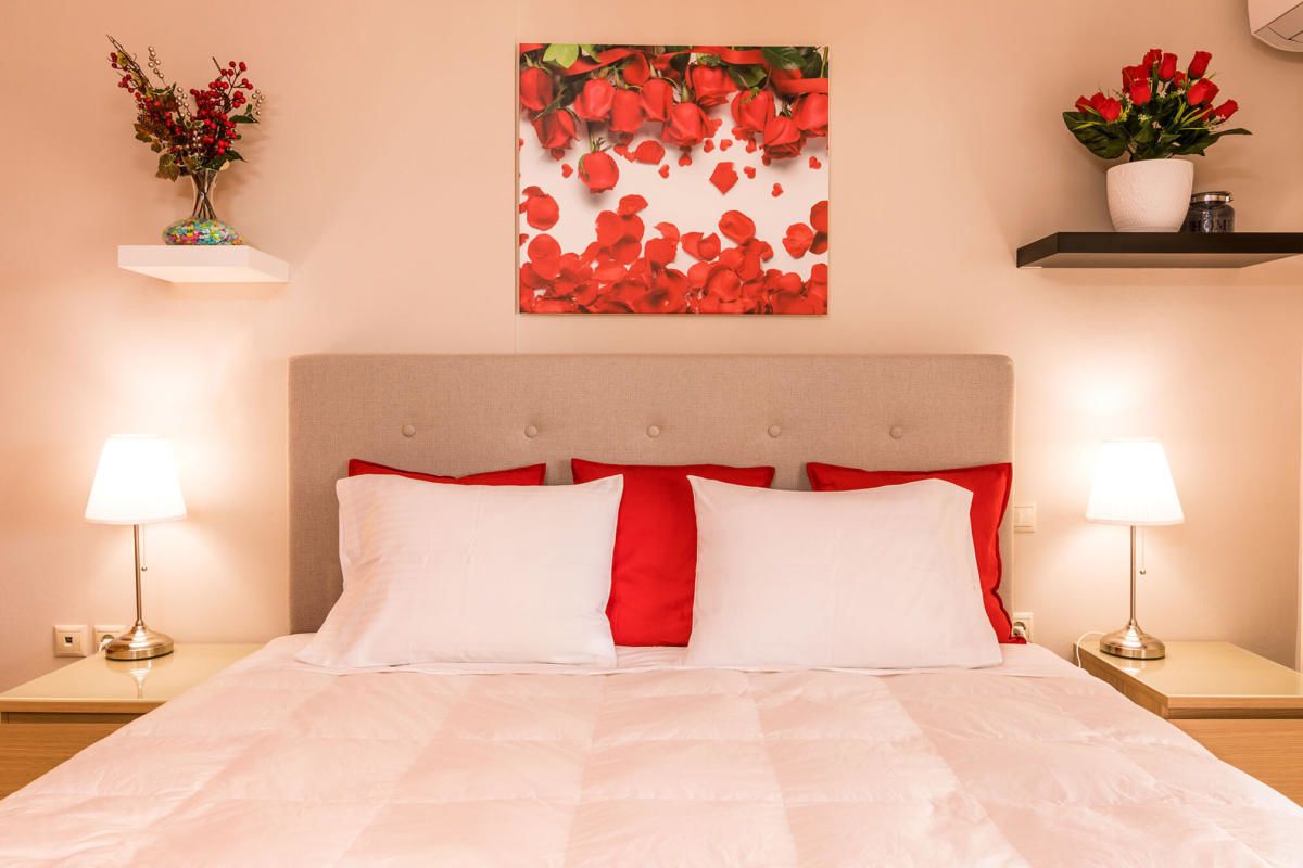 A neatly made bed with white and red bedding, two bedside lamps, and a wall-mounted artwork of red roses.