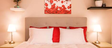 A neatly made bed with white and red bedding, two bedside lamps, and a wall-mounted artwork of red roses.