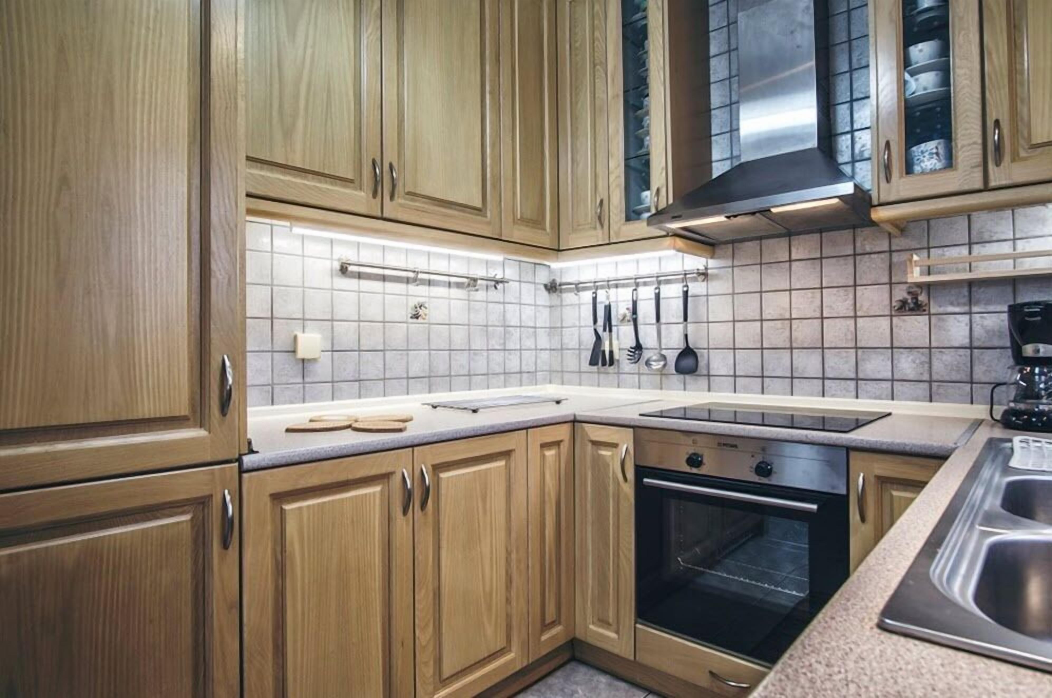 Una cucina con mobili in legno, un lavandino in acciaio inossidabile, un forno integrato e una parete di fondo rivestita di piastrelle.