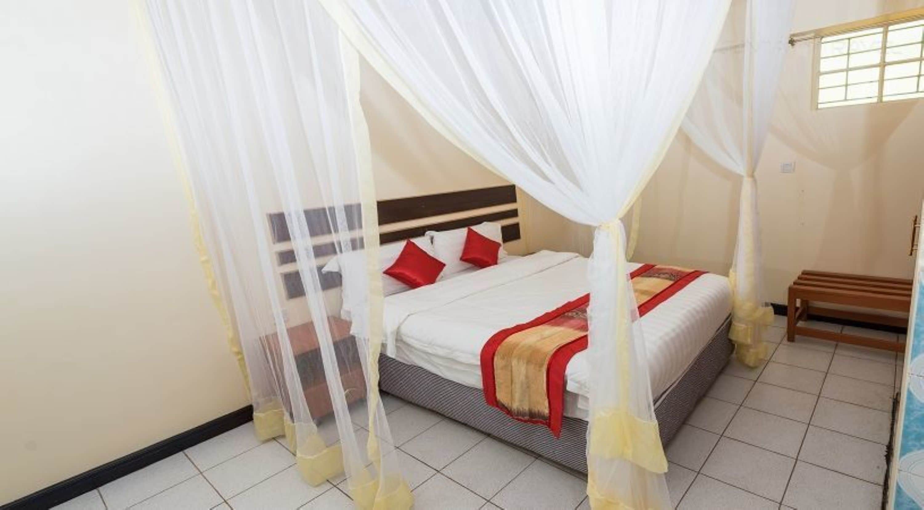 A bed with a canopy, a bench, and a window with bars.