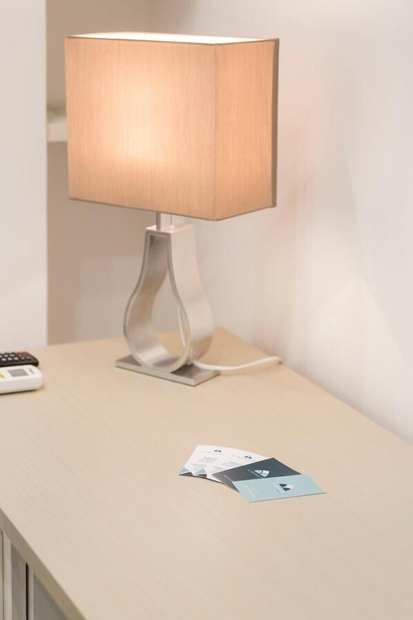 Une lampe de table moderne, dotée d’un pied métallique et d’un abat-jour rectangulaire, posée sur une table en bois de couleur claire.
