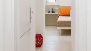 A narrow hallway leading to a bedroom with a bed, a window, and a bedside table. - Il Vicoletto (Amalfi)