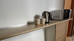 A kitchenette with a microwave, a coffee maker, and two cups on a shelf. There are two white stools in front of a patterned floor. - Il Vicoletto (Amalfi)