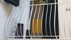 A balcony with a white railing and a black door with a green shutter. - Il Vicoletto (Amalfi)
