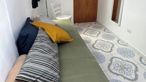 A narrow hallway with a bed, a chair, and a door. - Il Vicoletto (Amalfi)