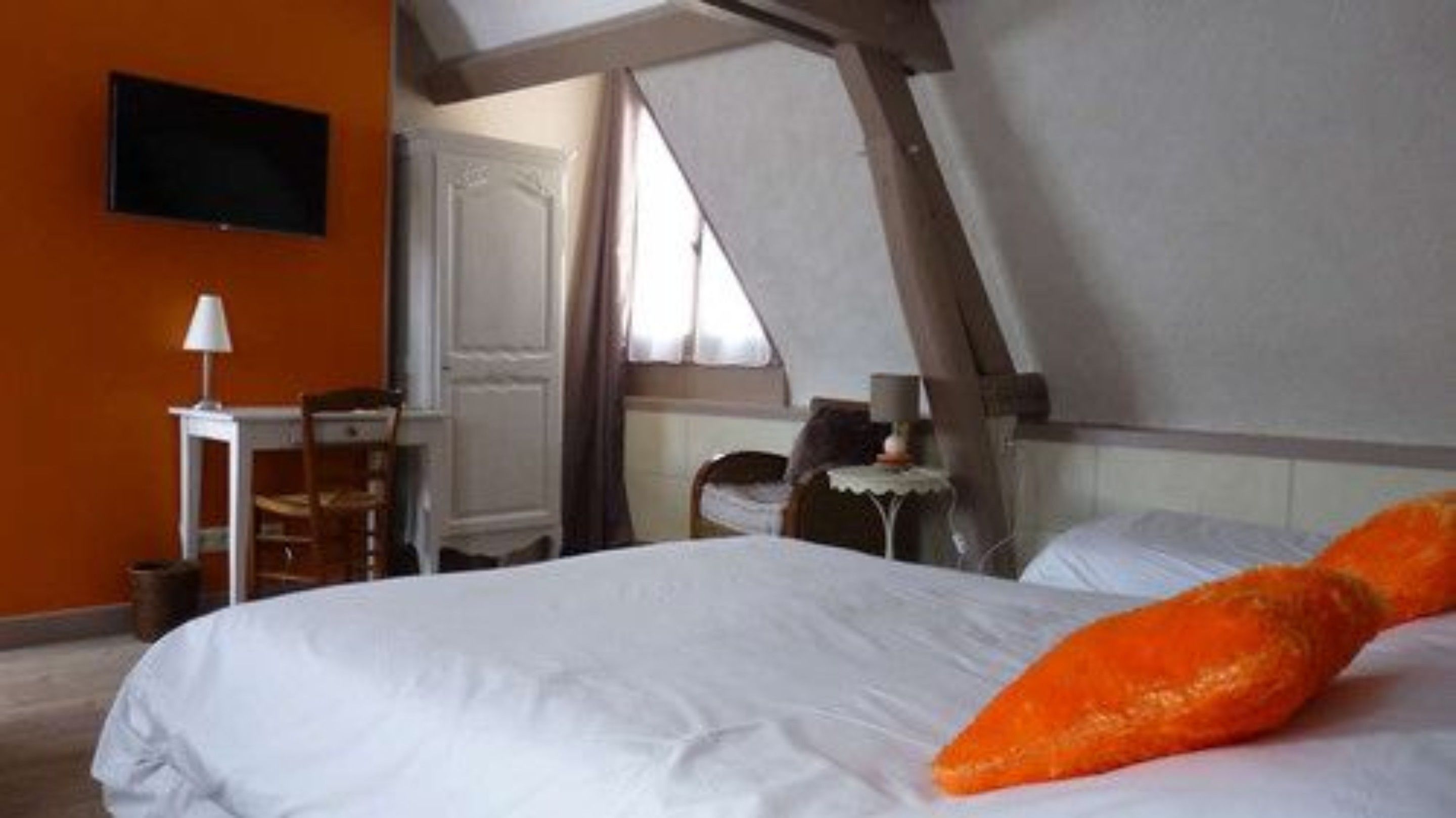 A bedroom with a bed, a chair, a small table, and a television on the wall.