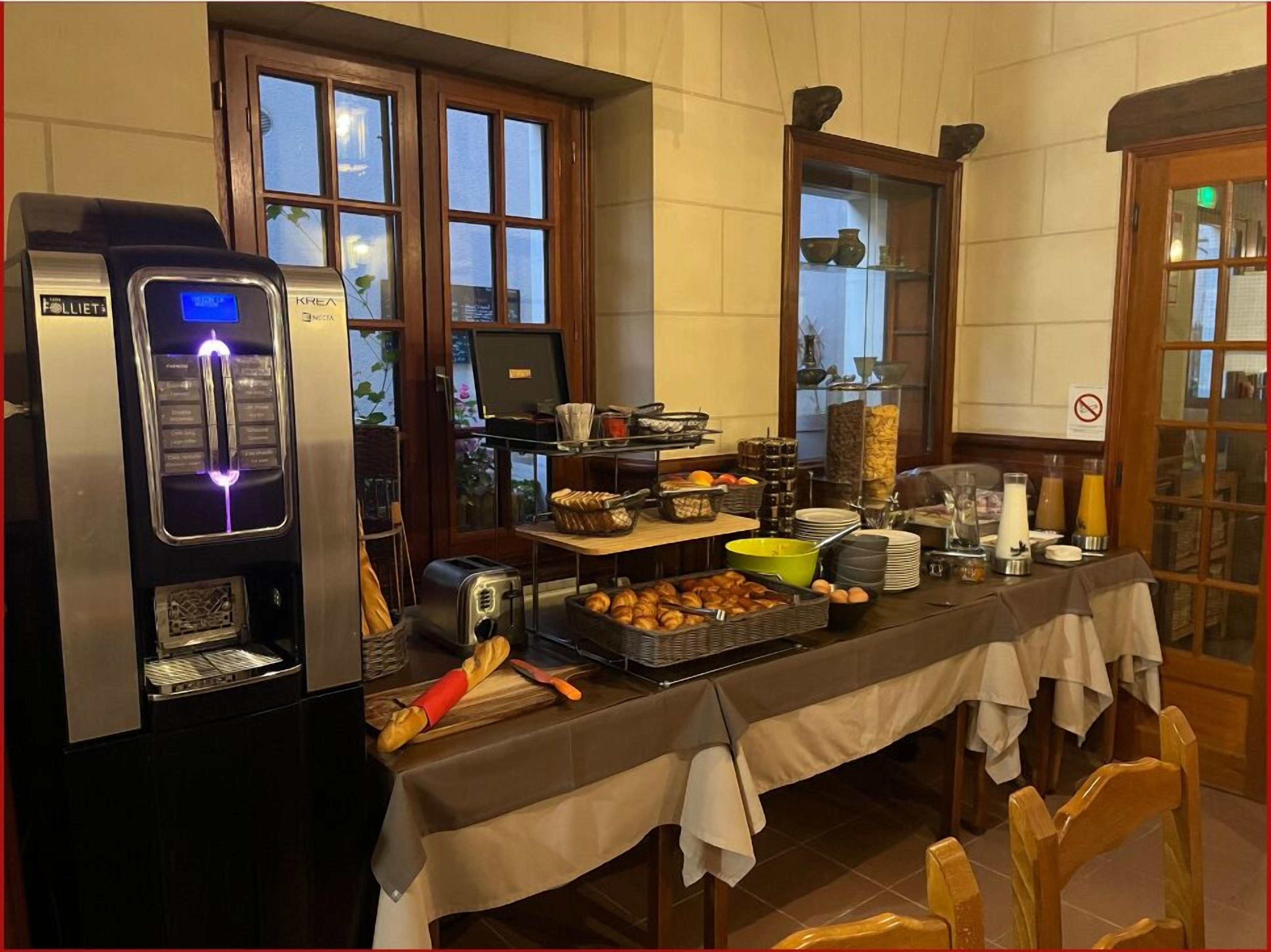 Disposição de buffet de café da manhã, com máquina de café, torradeira e diversos alimentos sobre uma mesa.