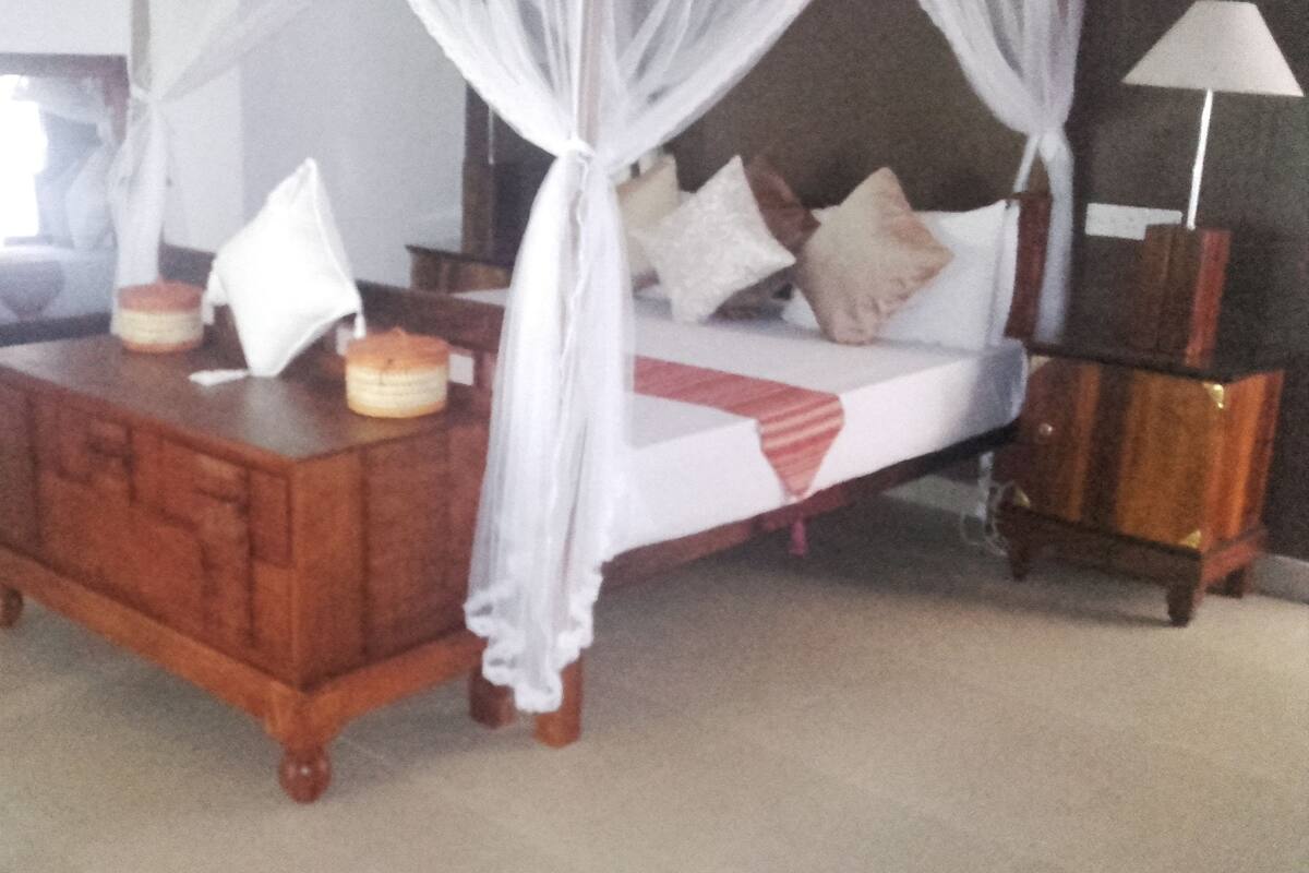 Una cama con dosel, un aparador de madera, una lámpara y un televisor.
