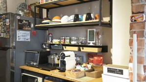A compact kitchen with a refrigerator, microwave, toaster, and a coffee machine. There are shelves above holding dishes and jars. - Lento Hostel (Tainan)