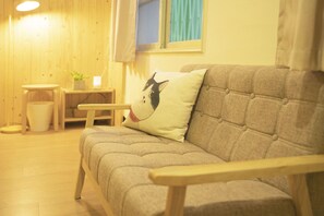 A cozy living room with a sofa, a small table, a potted plant, and a window with curtains.