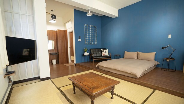 A room with a bed, a TV, a coffee table, and a blue wall. - Lento Hostel (Tainan)
