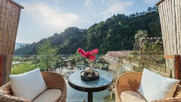 A balcony with wicker chairs and a small table, overlooking a lush green landscape and a river.