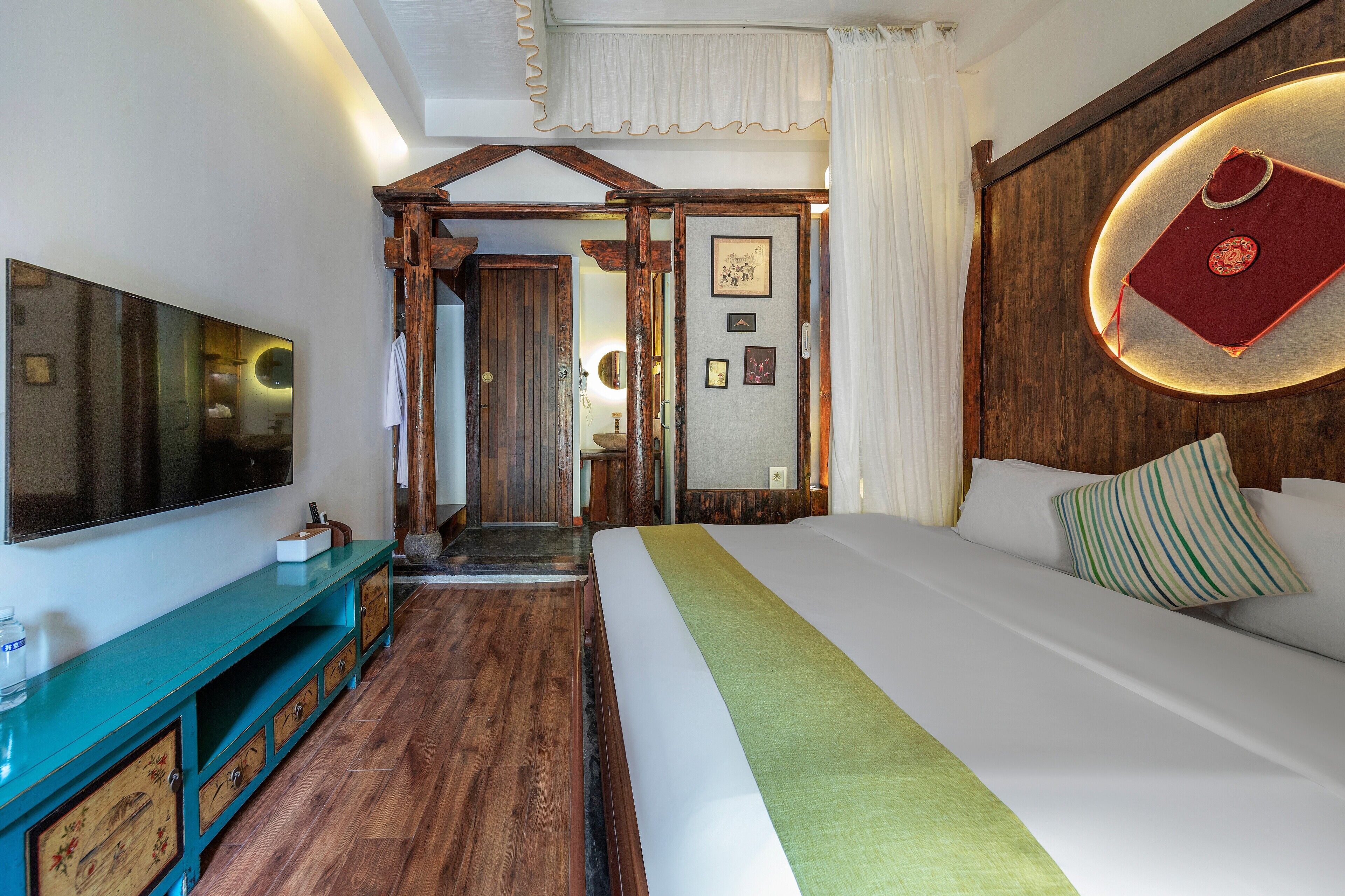 A bedroom with a large bed, a TV mounted on the wall, a wooden cabinet, and a mirror.