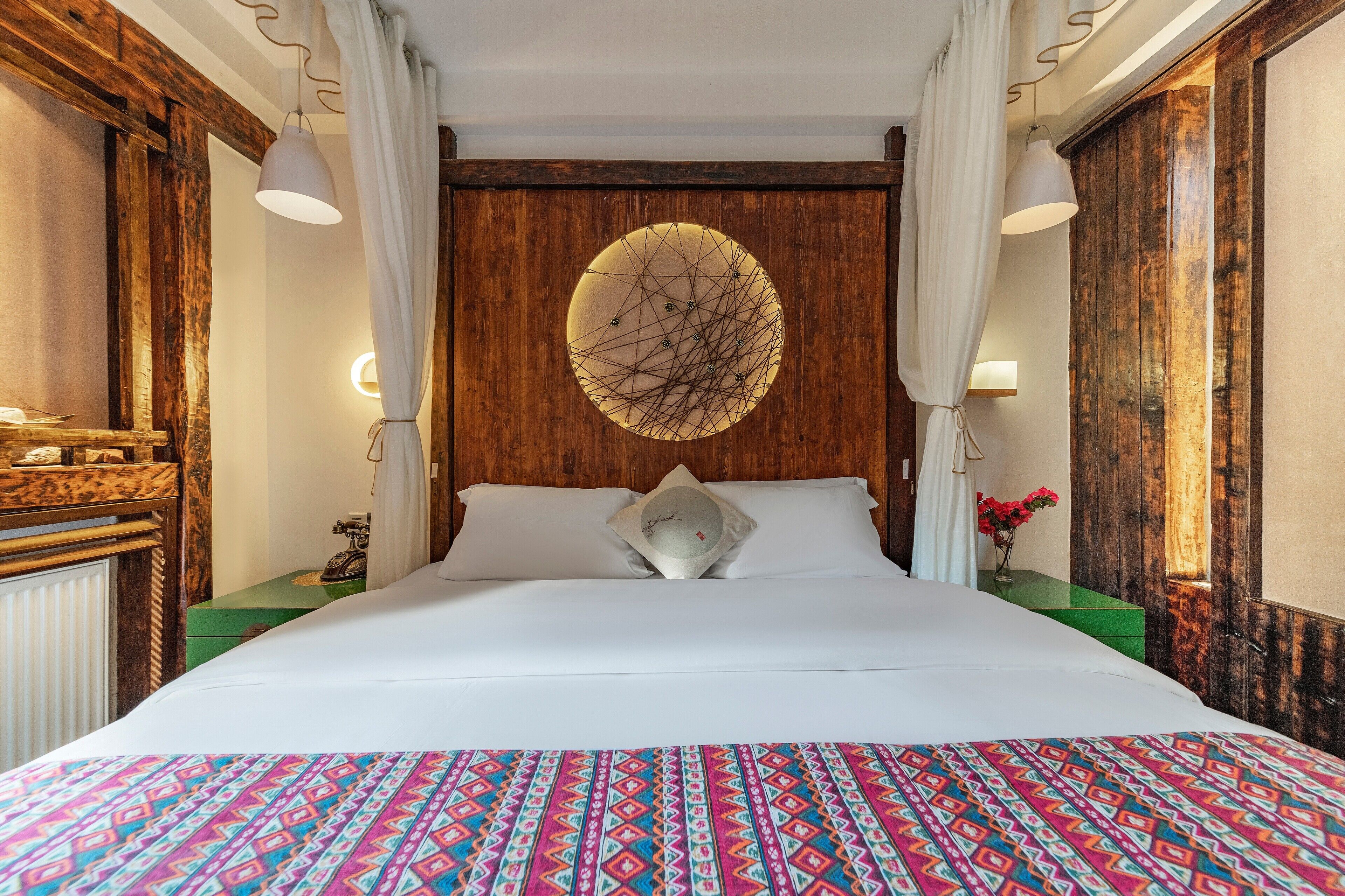Habitación de hotel con una cama grande, cabecero de madera, un adorno en la pared y una mesita de noche verde con un florero.