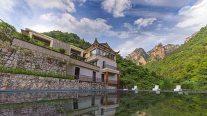 A multi-story building with a stone retaining wall and a reflective pool. - Pandora Vista Retreat  (Zhangjiajie)