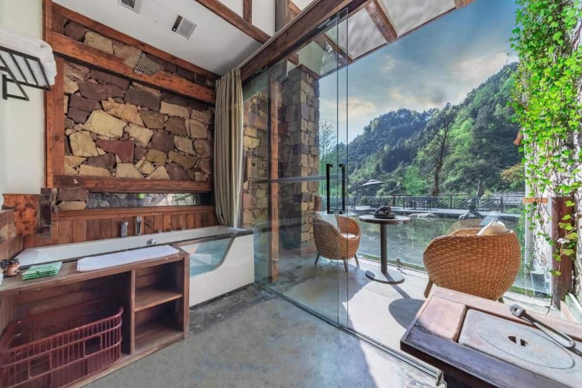 Habitació moderna amb una paret de pedra, una porta de vidre que dona a un balcó amb vista a una zona boscosa.