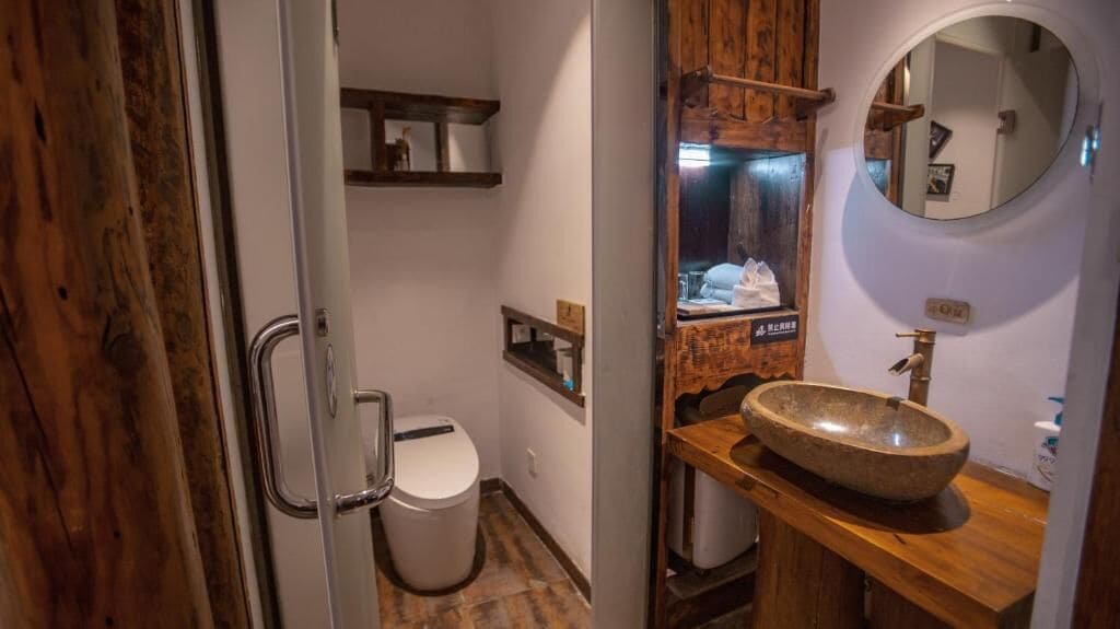 Un baño con tocador de madera, un espejo redondo y un inodoro.