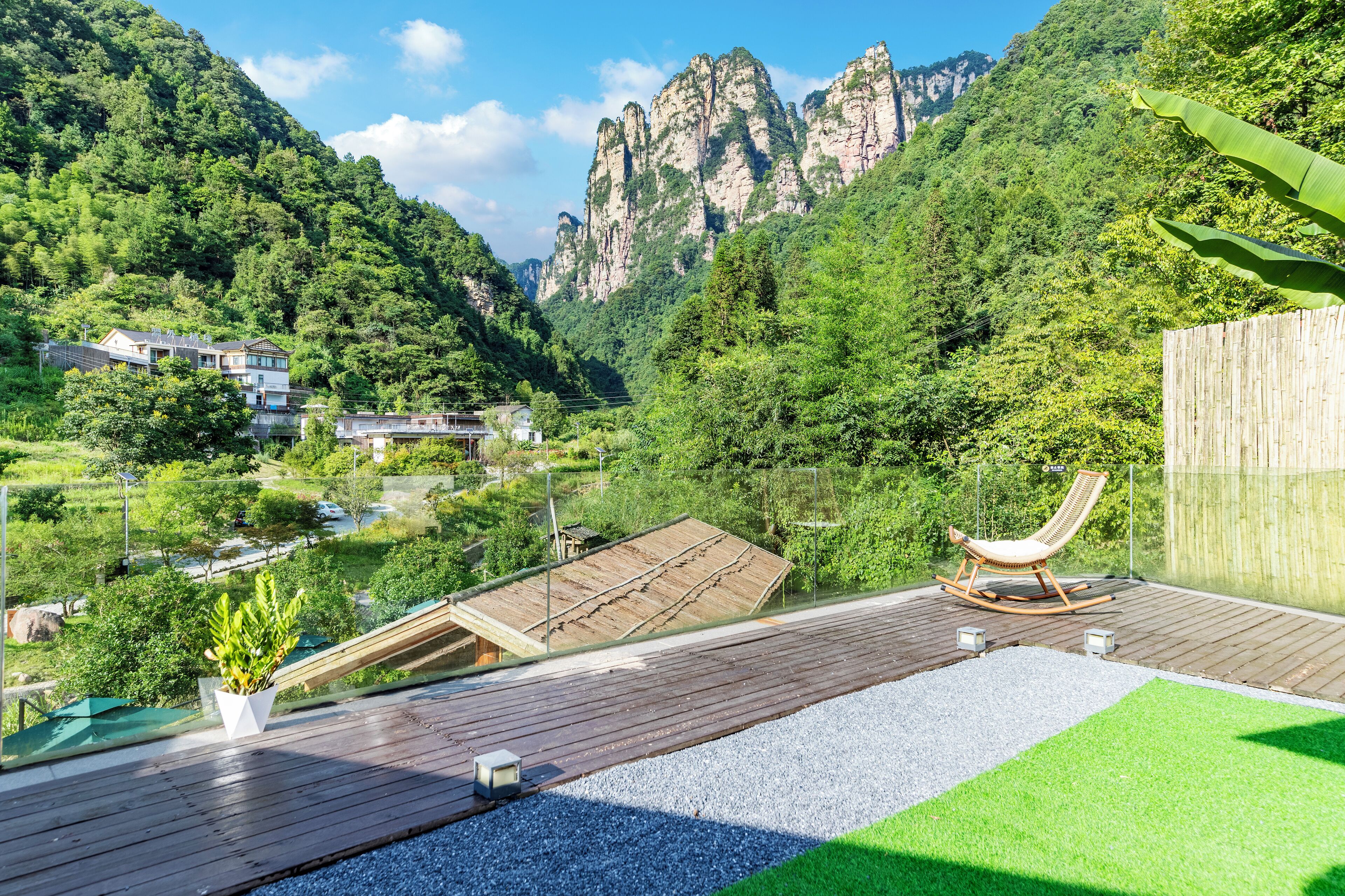 Une terrasse en bois avec un fauteuil à bascule, un petit jardin et une vue sur un paysage montagneux.