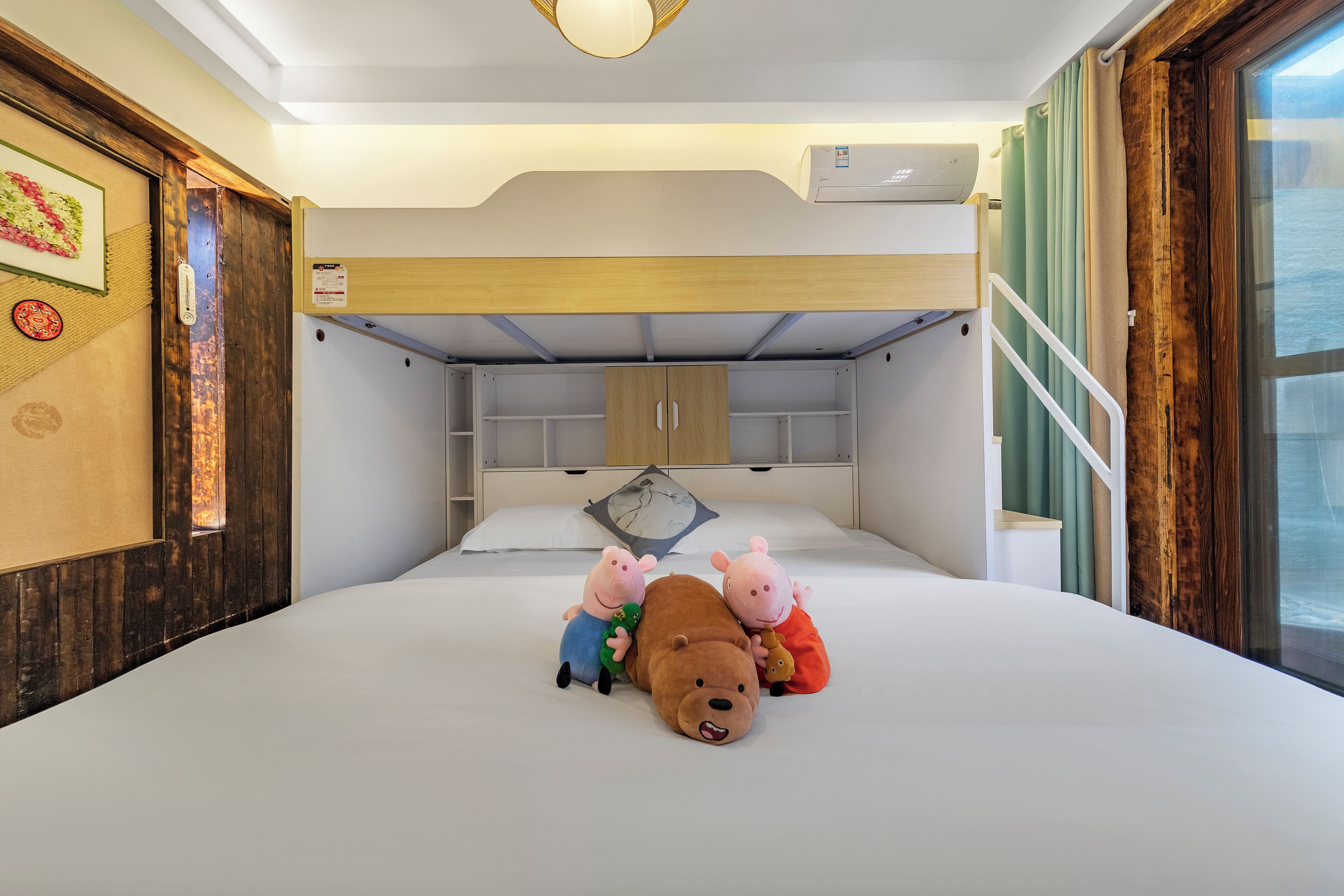 A bedroom with a bunk bed, a bed with plush toys, a wooden headboard, a window with curtains, and a wall-mounted air conditioner.