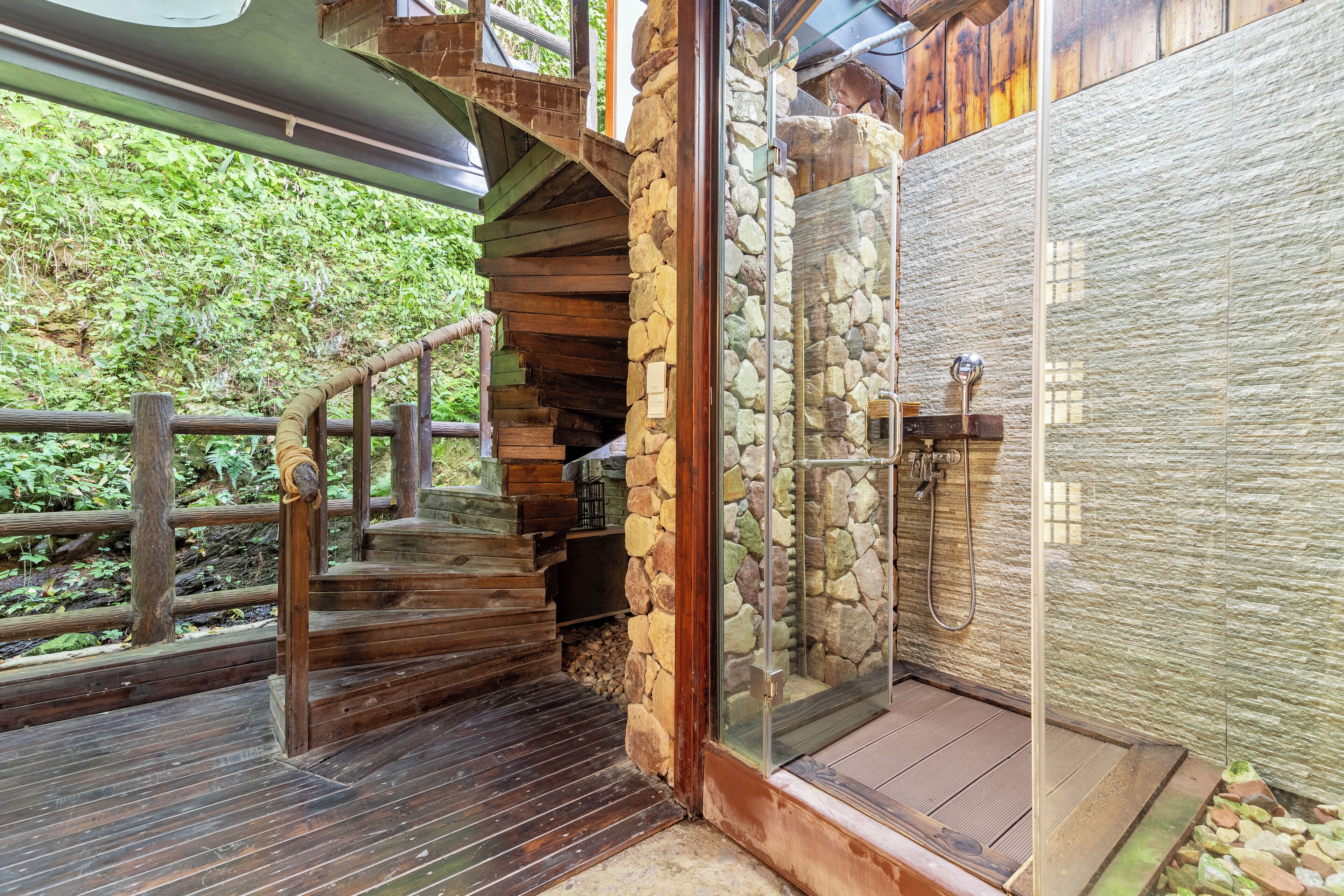 A wooden staircase leading to a stone-walled shower area with a glass door.