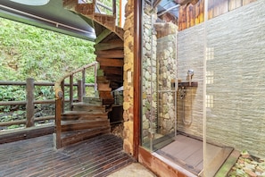 A wooden staircase leading to a stone-walled shower area with a glass door.