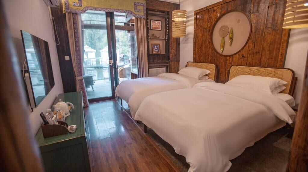 Habitación de hotel con dos camas, un panel de pared de madera, una mesita con una tetera y vistas a través de un ventanal.