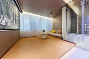 A modern living room with a wooden floor, a round coffee table with a plant, a sofa with cushions, and a large poster on the wall.