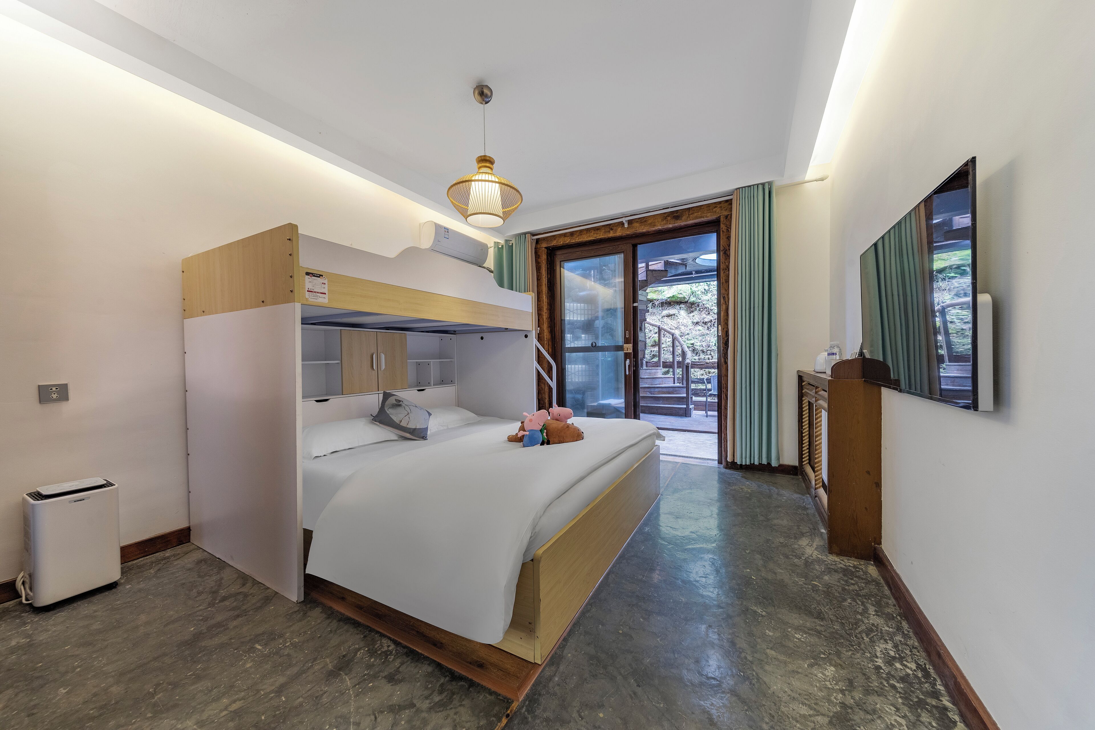 A compact hotel room with a bunk bed, a small kitchenette, a single bed with a white comforter, and a large window with curtains.