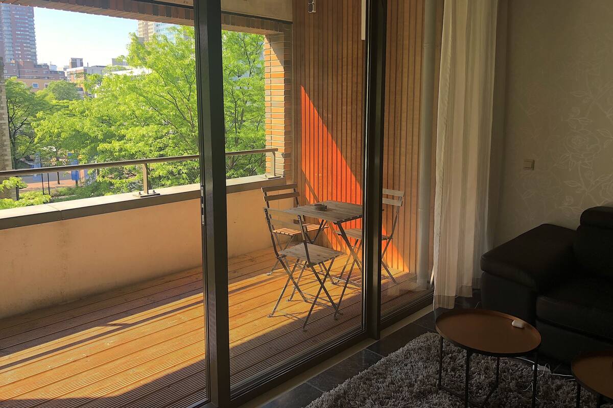 Un balcón con vistas a árboles y edificios, una silla plegable, una mesita y un sofá.