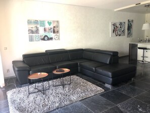 A modern living room with a black sectional sofa, two small round tables, and a shaggy rug. - MyCityLofts - Meent (Rotterdam)