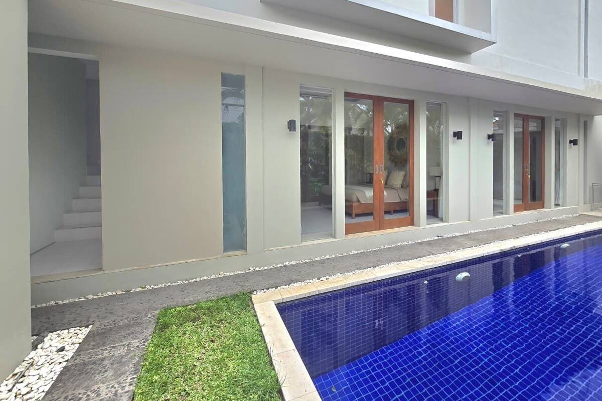 A modern house with a swimming pool, a staircase, and a door leading to a covered outdoor area.