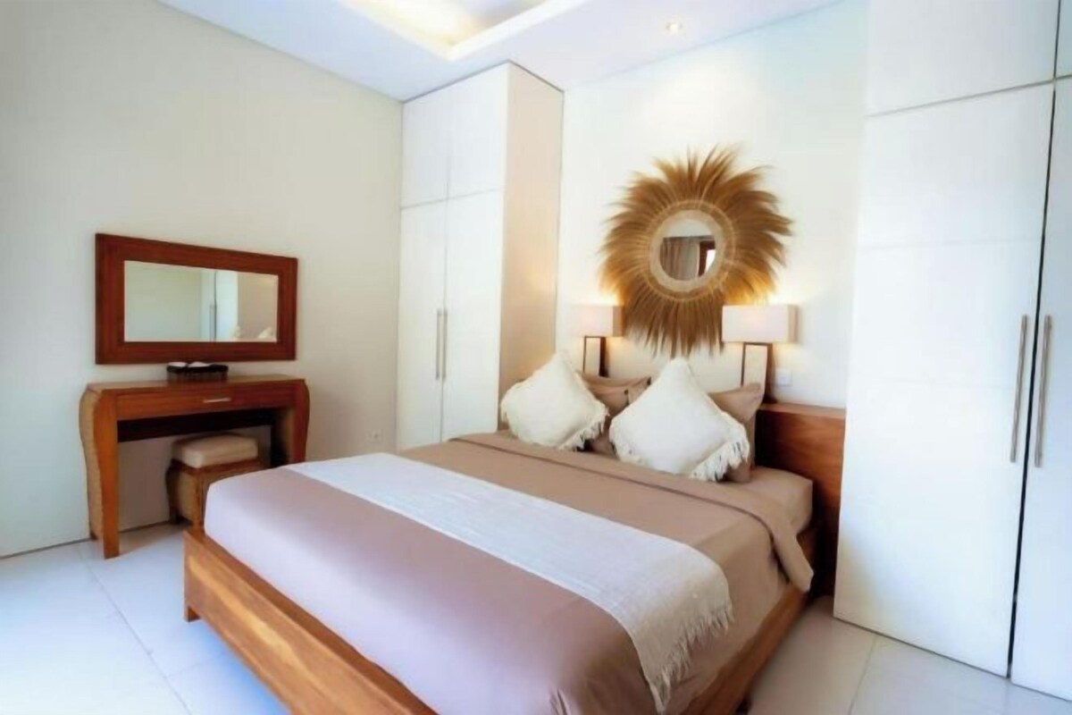 A modern bedroom with a large bed, a wooden desk, a mirror, and a unique wall decoration.