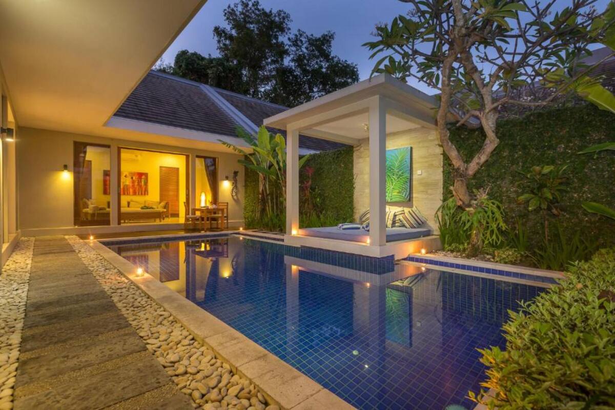 A modern pool area with a clear pool, a covered seating area, and a well-lit interior space.