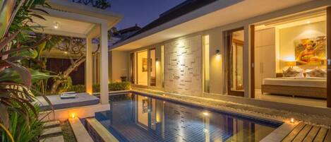 A modern house with a swimming pool, a covered patio, and a well-lit interior.